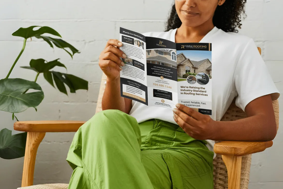 A person holding a RISE Roofing & Restoration brochure showing the brand system and project photography.